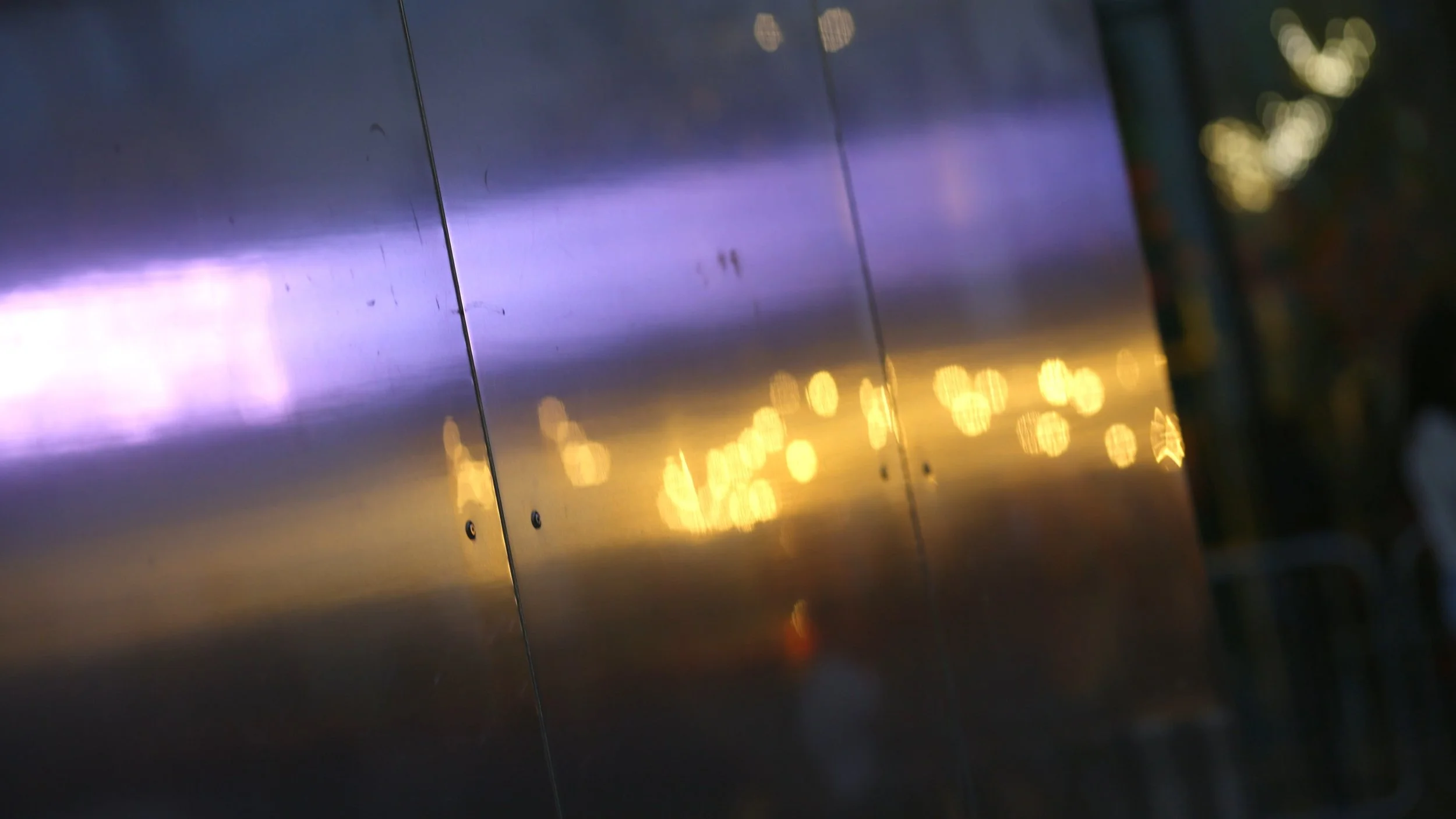 Close-up of a reflective metal surface with bokeh light reflections, possibly taken outdoors during sunset or dusk.
