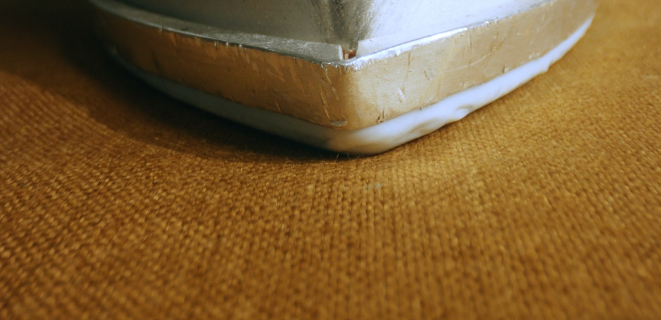 Close-up of the bottom corner of a stainless steel tray or baking dish on a textured brown surface.