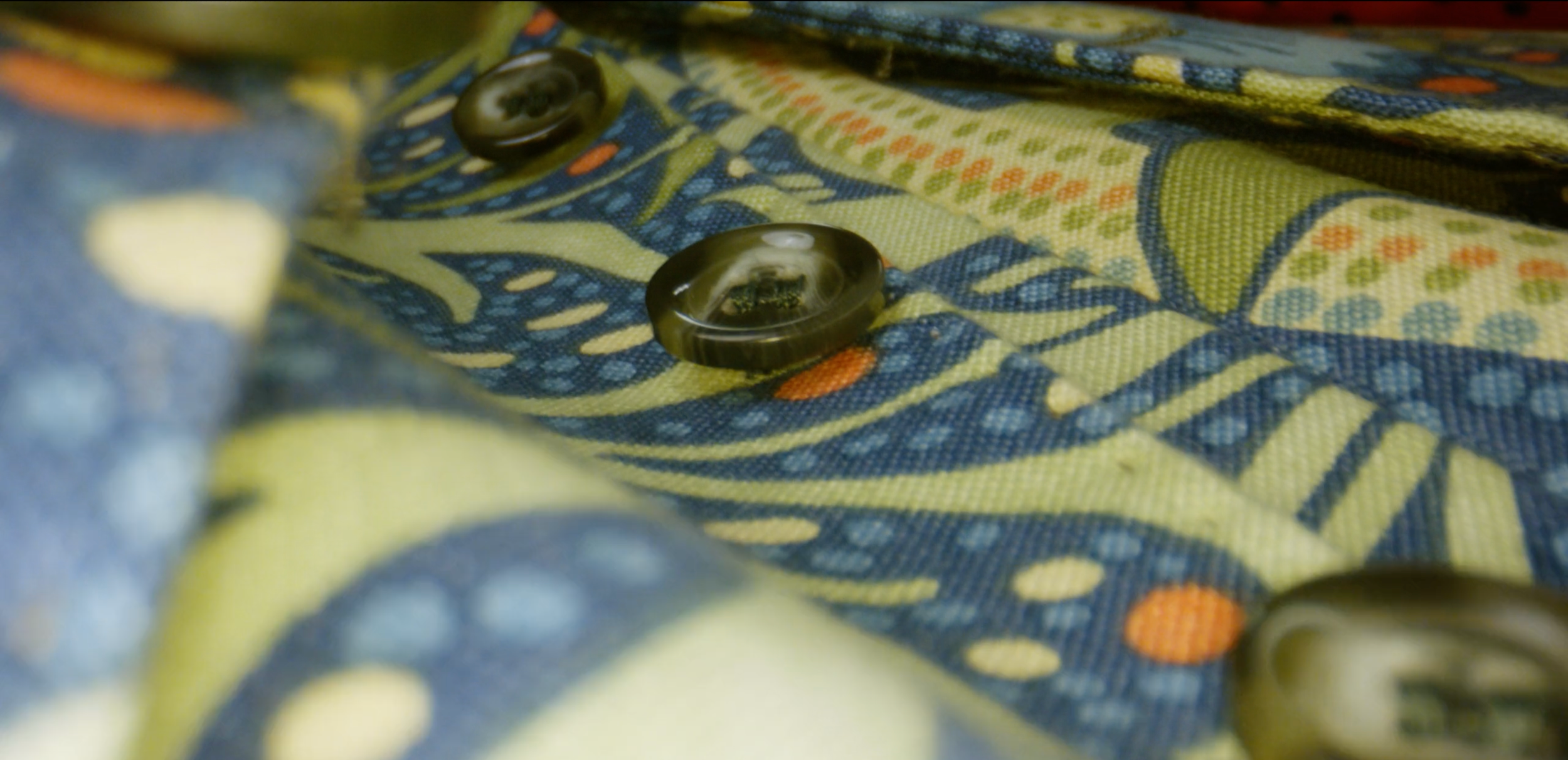 Close-up of a fabric with a colorful, intricate pattern featuring blue, yellow, and orange details, with a few dark buttons attached.