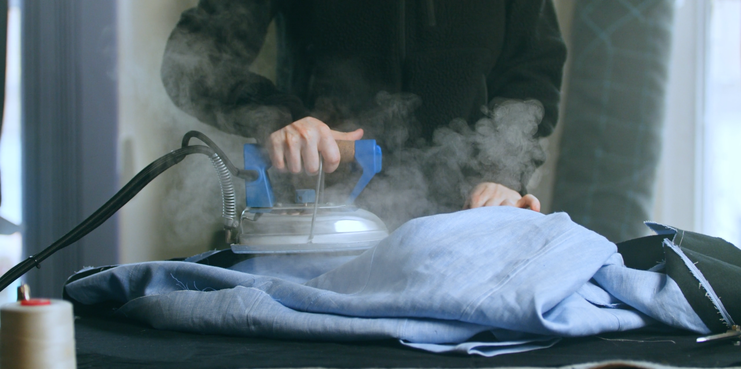 Person using a handheld steamer to remove wrinkles from a light blue shirt on a flat surface.