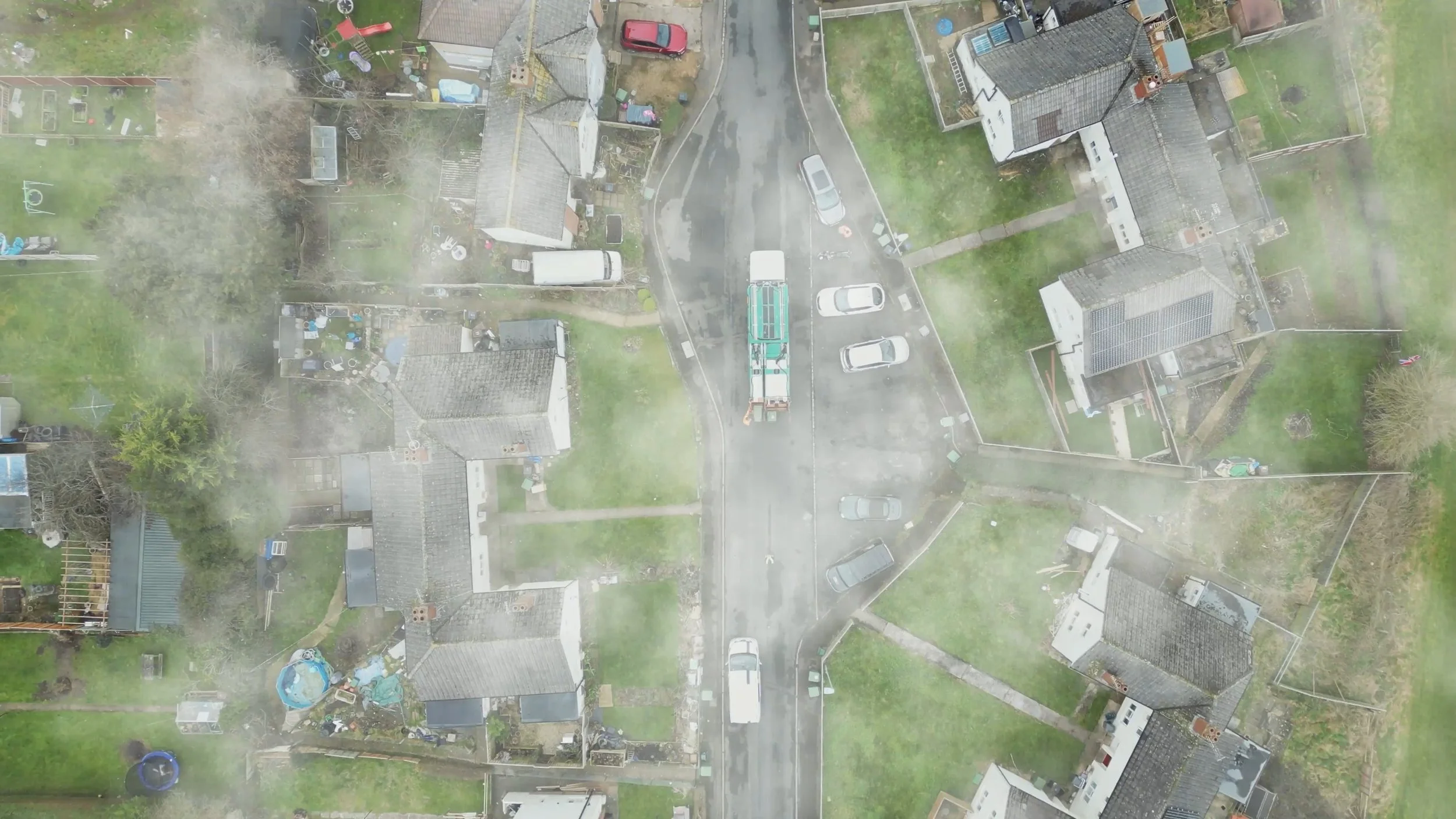 An aerial view of a residential neighborhood with houses, yards, and cars, viewed through a window with condensation or fog.