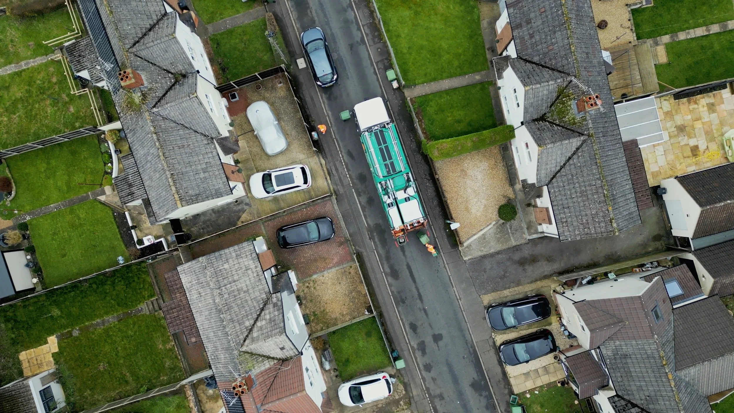 An aerial view of a street with parked cars, houses, and a utility truck working on the road.