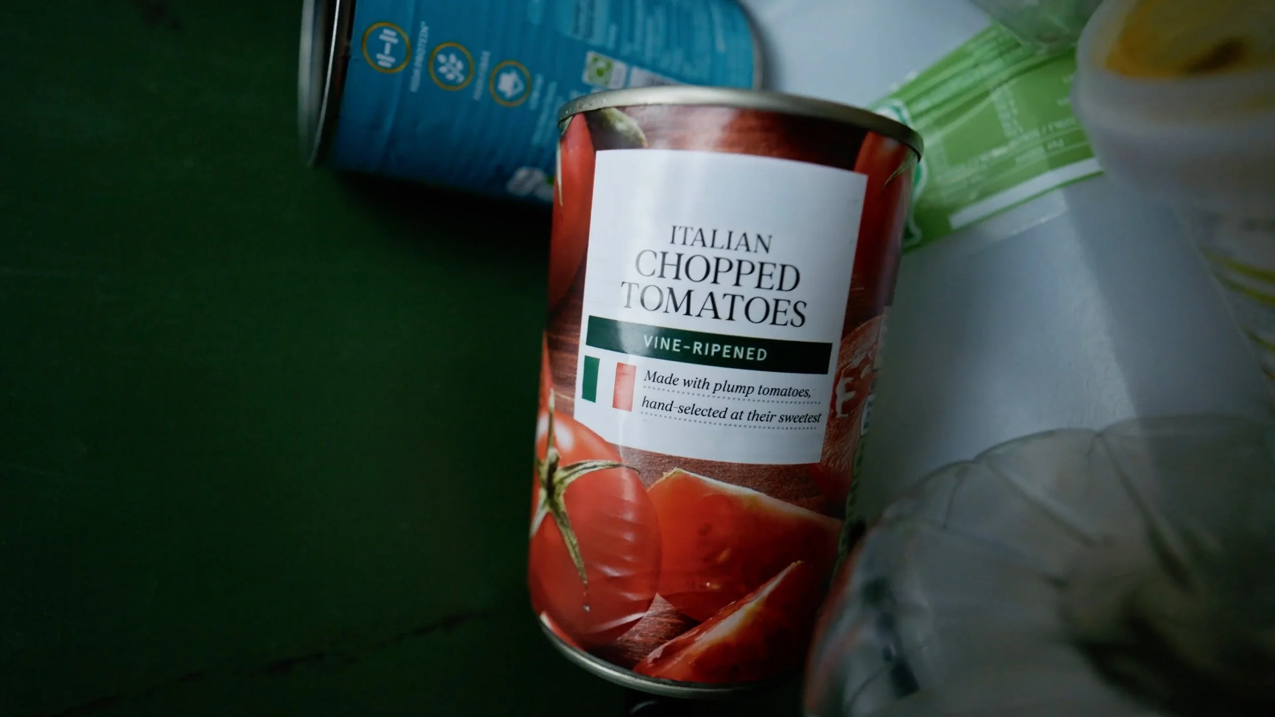 A can of Italian chopped tomatoes with vine-ripened label, showing images of tomatoes and positioned among other grocery items.