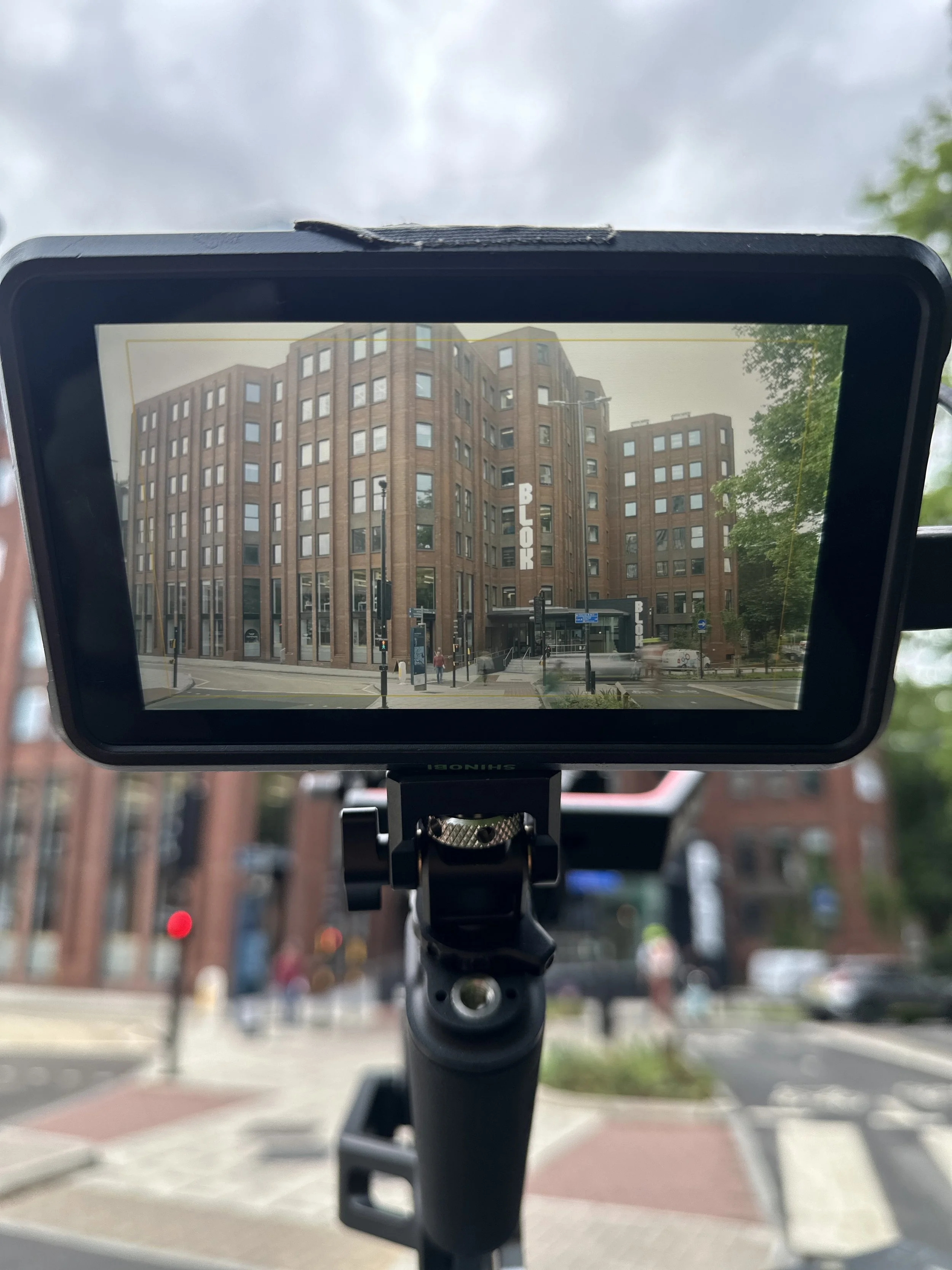 Photo of a brick building with the word 'BLOCK' on it, viewed through a camera or tablet screen on a tripod outdoors on a city street.