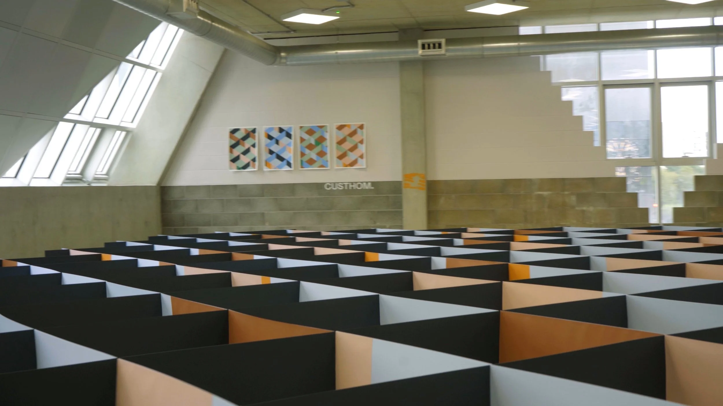 Empty, modern interior with patterned partitions in black, orange, and beige, and colorful geometric artwork on the wall.