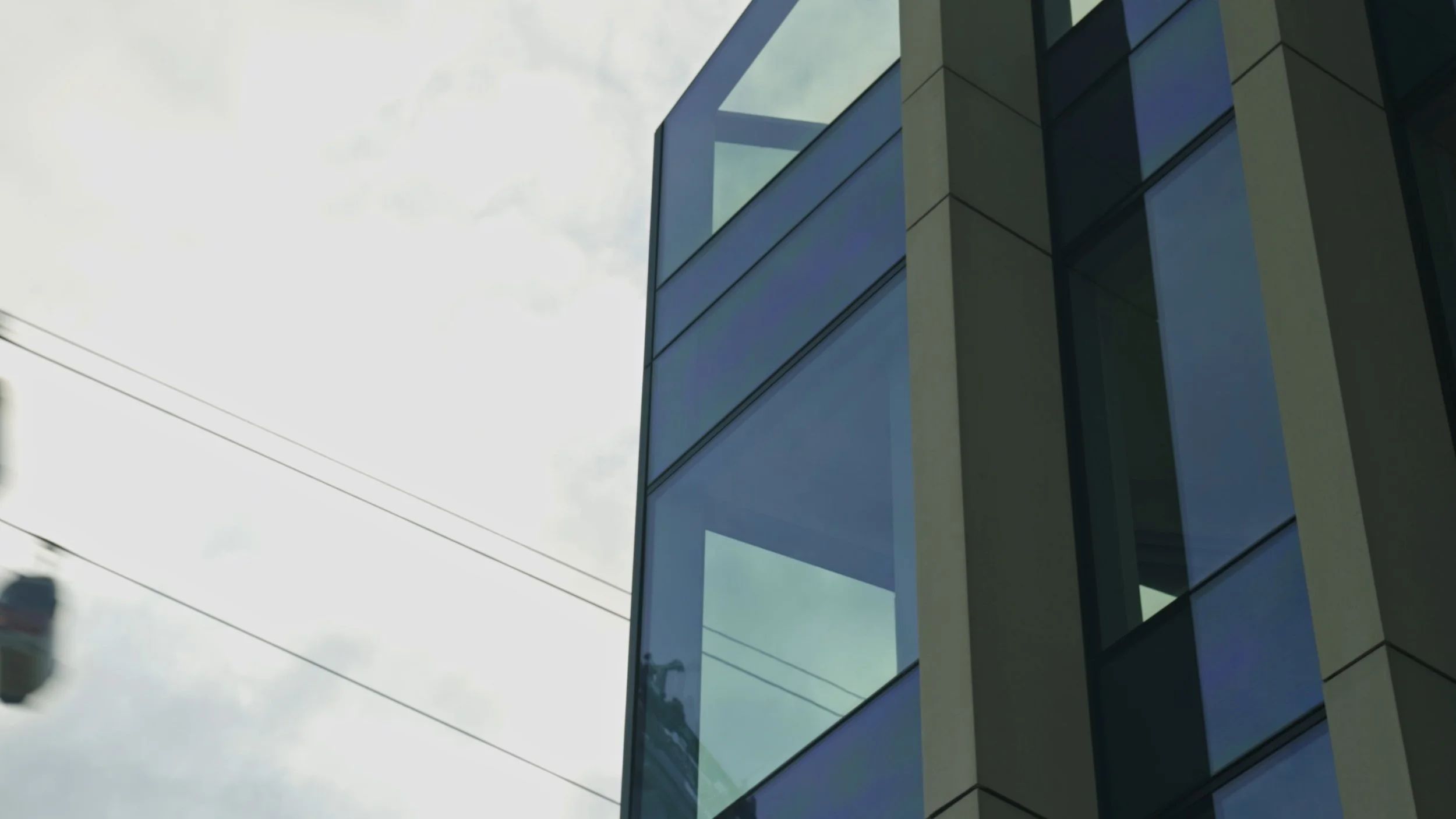 Close-up of a modern building with large glass windows and concrete panels, set against a cloudy sky with power lines.
