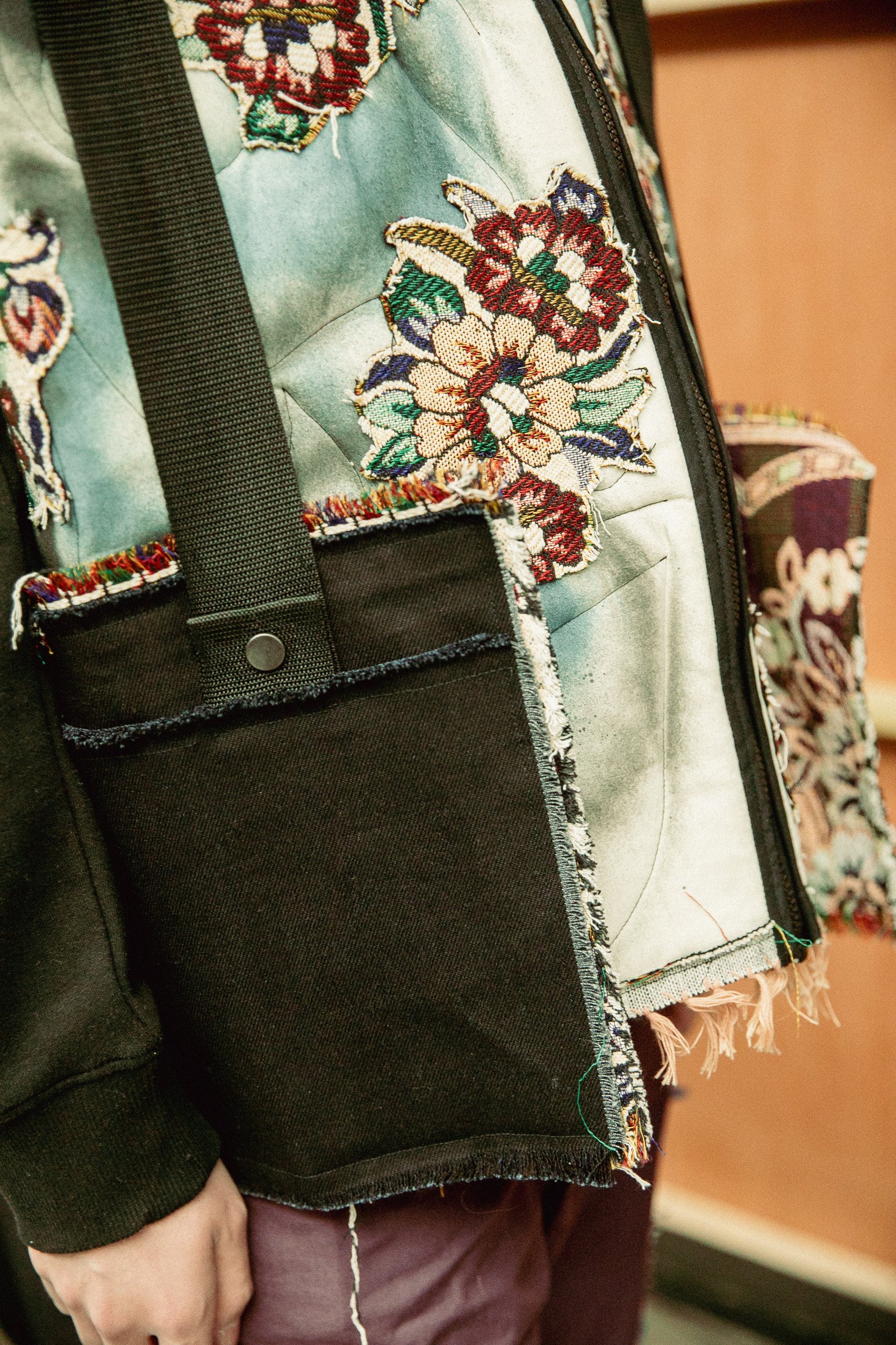 Close-up of a person wearing a quilted jacket with embroidered floral designs, with a black strap and pocket.