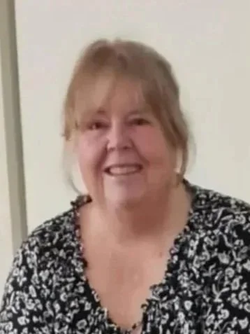 A woman with blonde hair smiling, wearing a black and white patterned top.