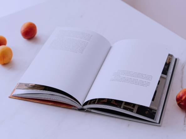 Libro abierto sobre una mesa blanca, rodeado de duraznos y manzanas.