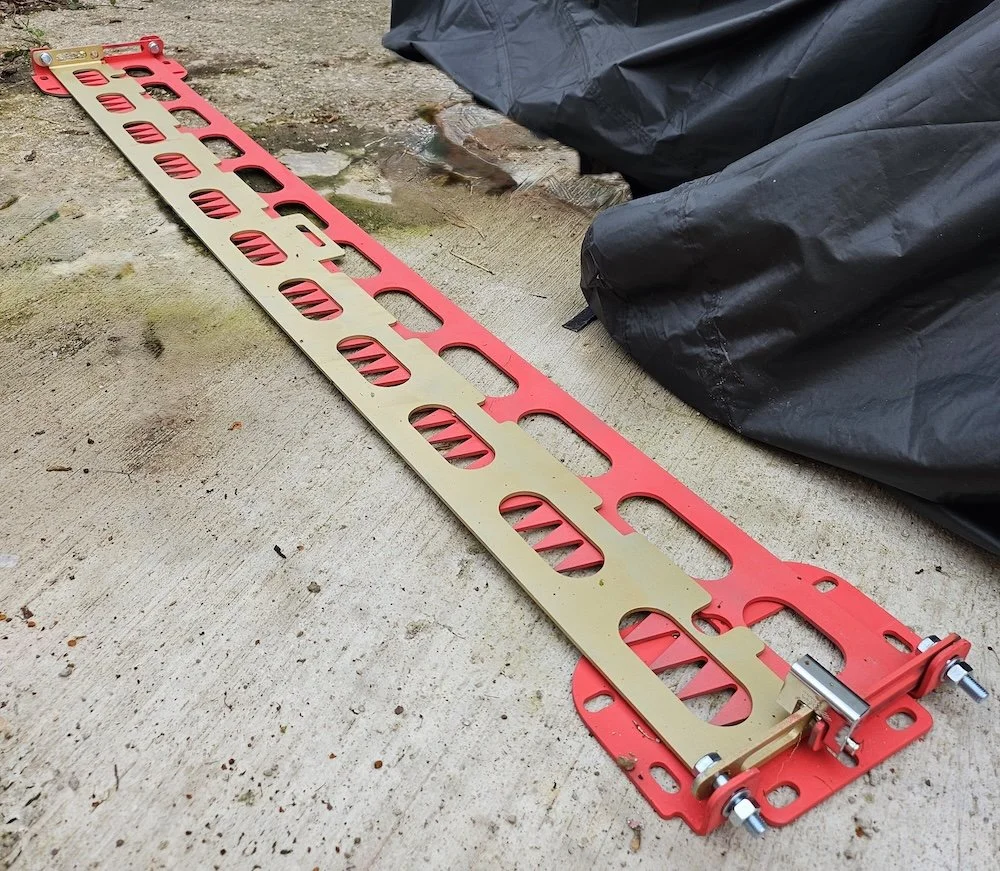 A long, orange and yellow metal tool lying on a concrete surface next to a black plastic bag.