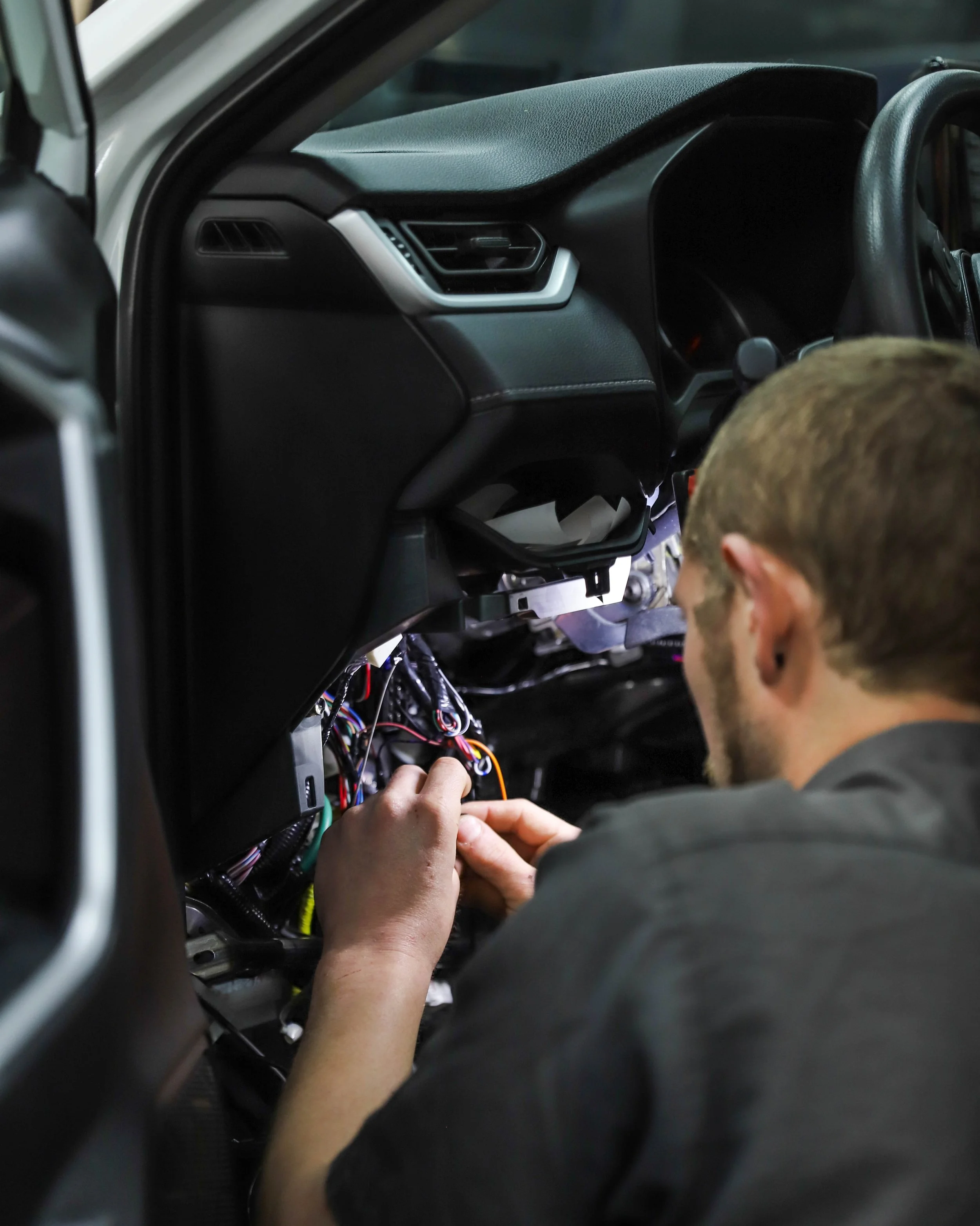 A man working on the wiring inside a vehicle's dashboard.