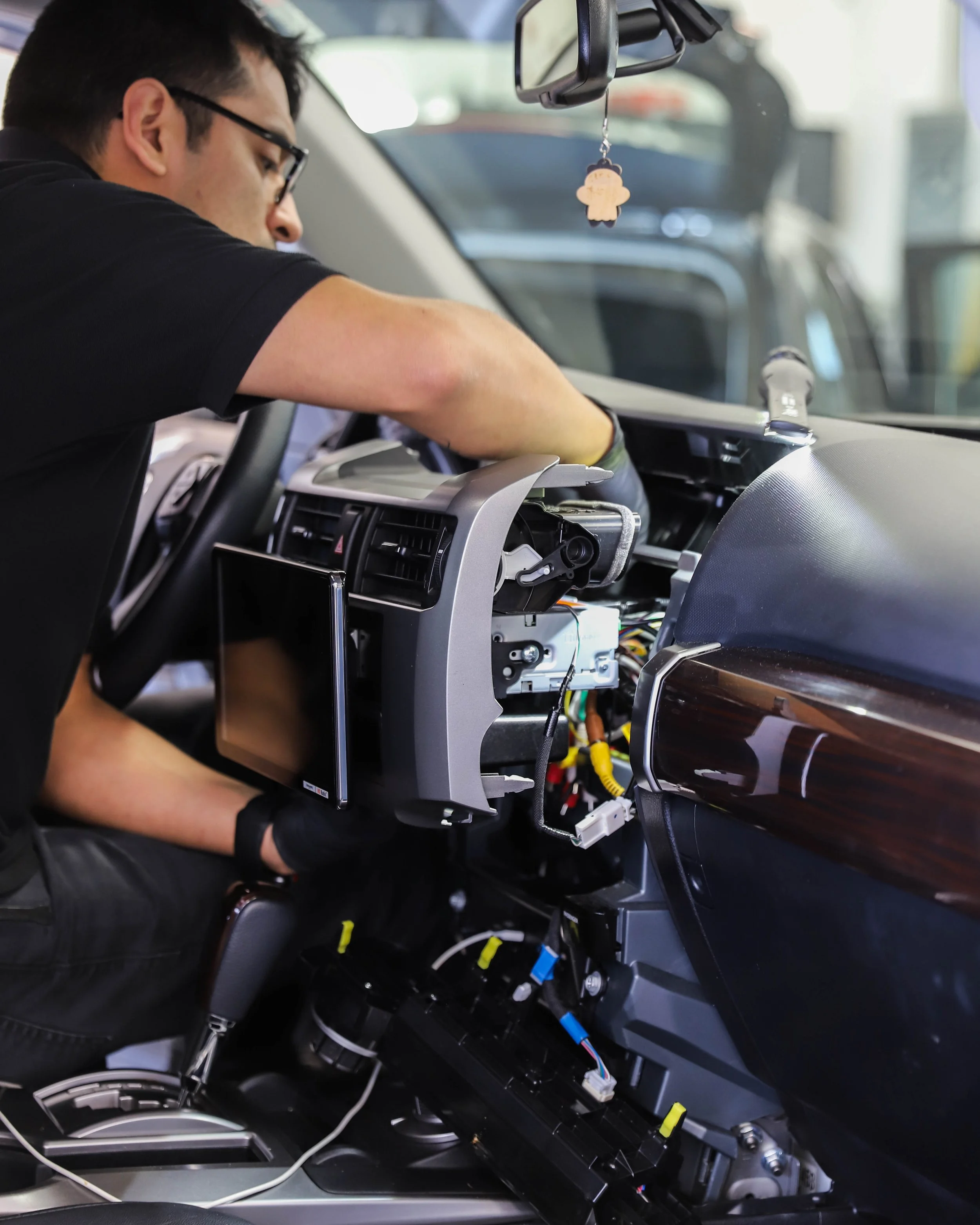 Man working on disassembled car dashboard, repairing or installing components inside the vehicle.