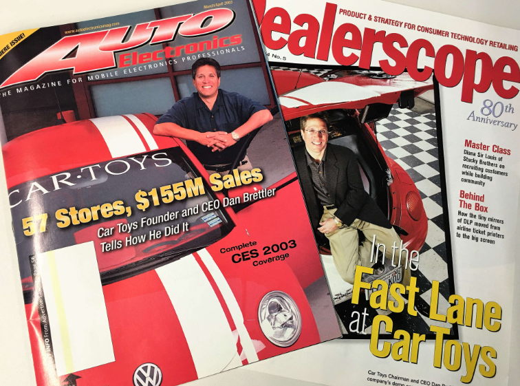 Two magazines, one titled 'Auto Electronics' with a cover photo of a man sitting on a red car toy, and the other titled 'ealscope' with a cover photo of a man sitting beside a real red sports car.