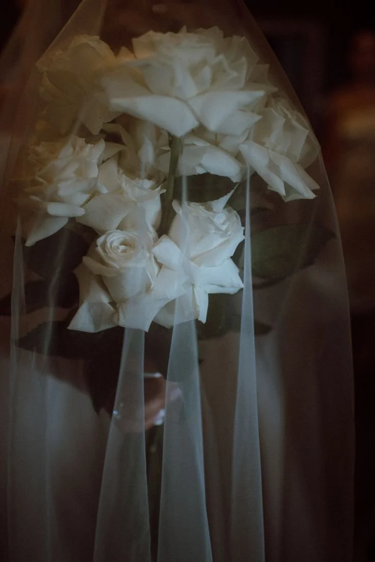 White roses wrapped in sheer fabric, likely a bouquet for a special occasion.