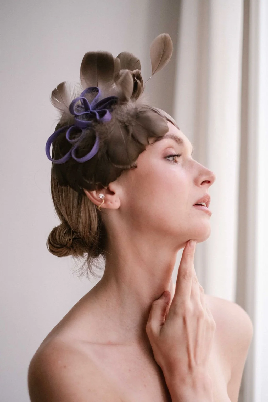 A woman with styled hair and feathered accessories on her head, thoughtfully touching her chin while looking to the side.