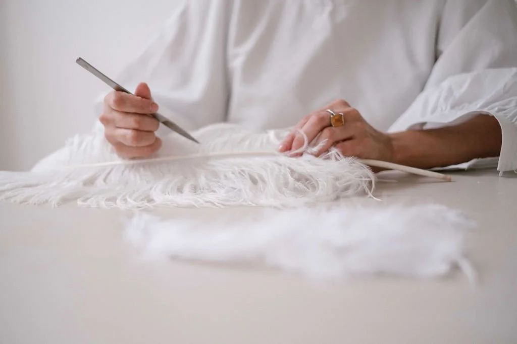 Person working with white fabric on a table, using a tool, possibly for textile or craft work.
