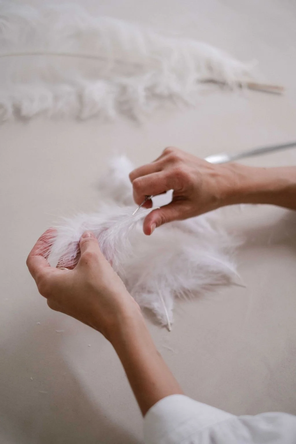 Hands sewing white feathered fabric with a needle, close-up view.
