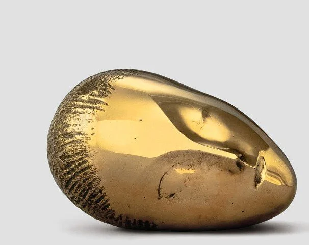 Close-up of a shiny, golden, metallic cowrie shell isolated on a white background.