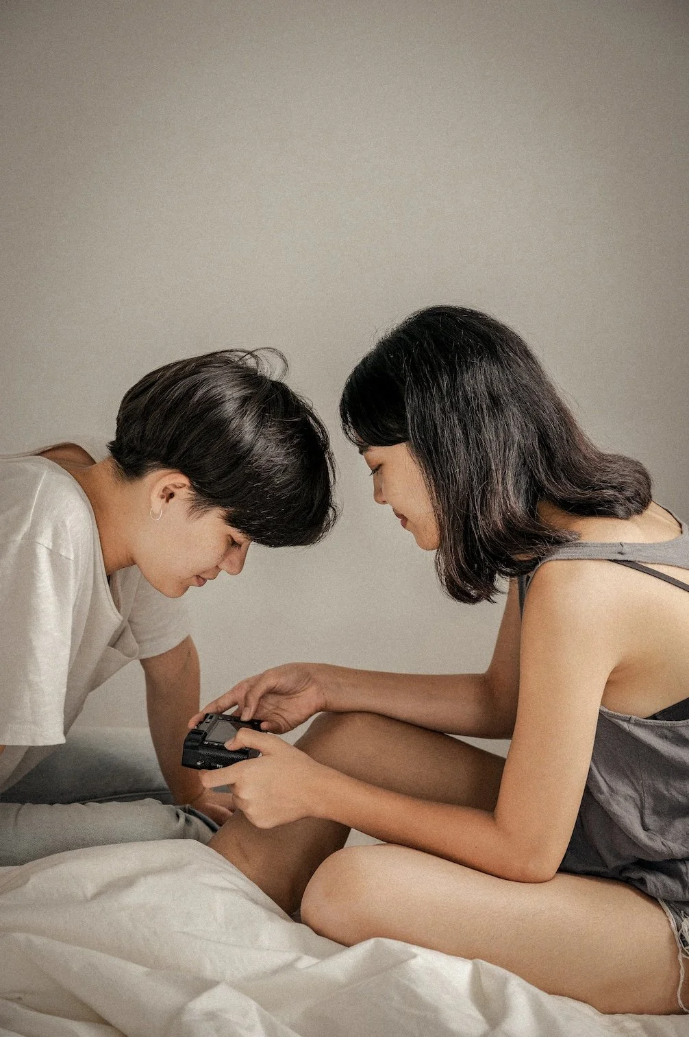 Two women sitting closely together on a bed, sharing a moment of connection and intimacy while looking at a camera.