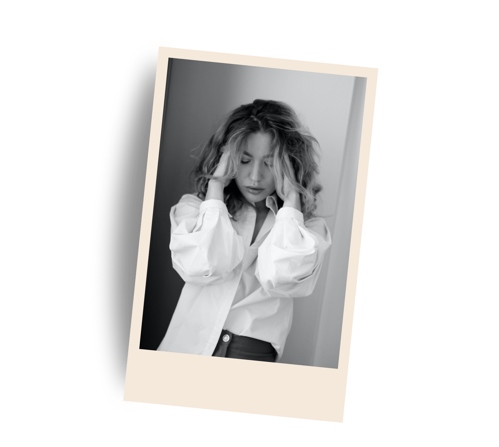 A black-and-white photo of a young woman with curly hair, wearing a white shirt, holding her head with both hands and looking down.