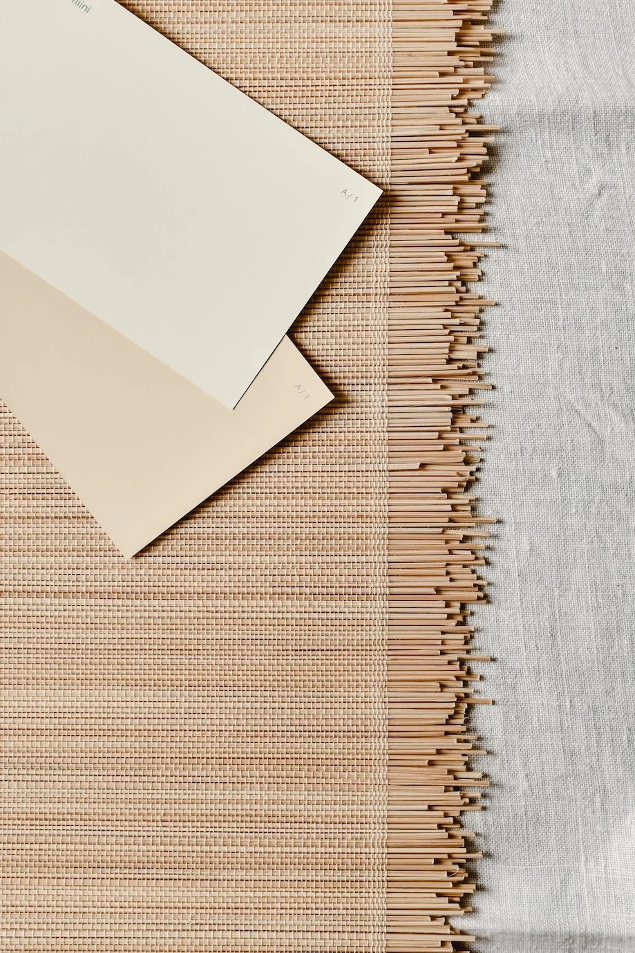 Two beige cards marked 'A 1/' lying on a woven beige mat with bamboo chopsticks along the edge, resting on a white fabric surface.
