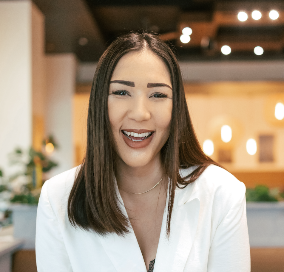 Smiling woman in a white top in a warm indoor setting, conveying openness, approachability, and emotional warmth