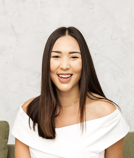 Smiling therapist with long dark hair seated in a comfortable chair against a neutral background