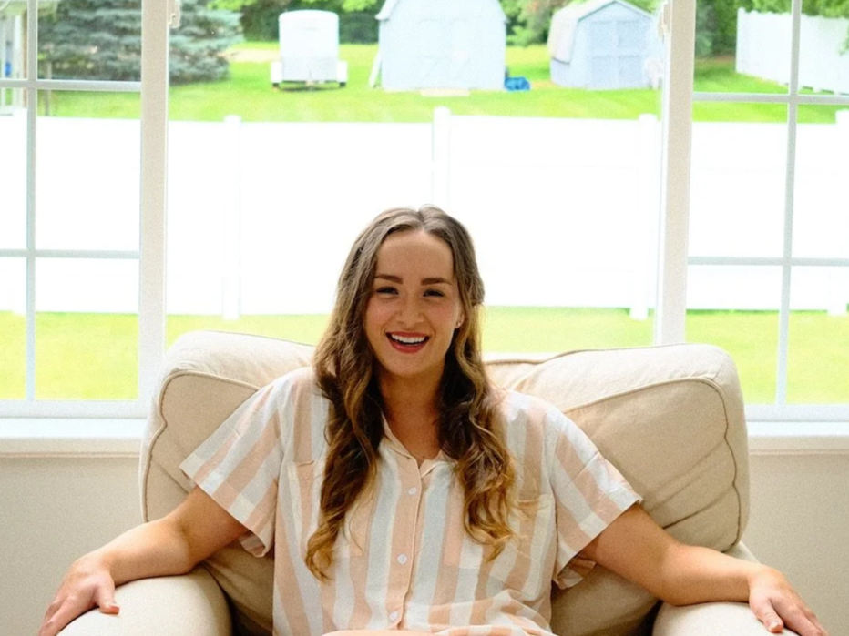 Therapist sitting on a light-colored couch in a bright, comfortable space with large windows and natural light