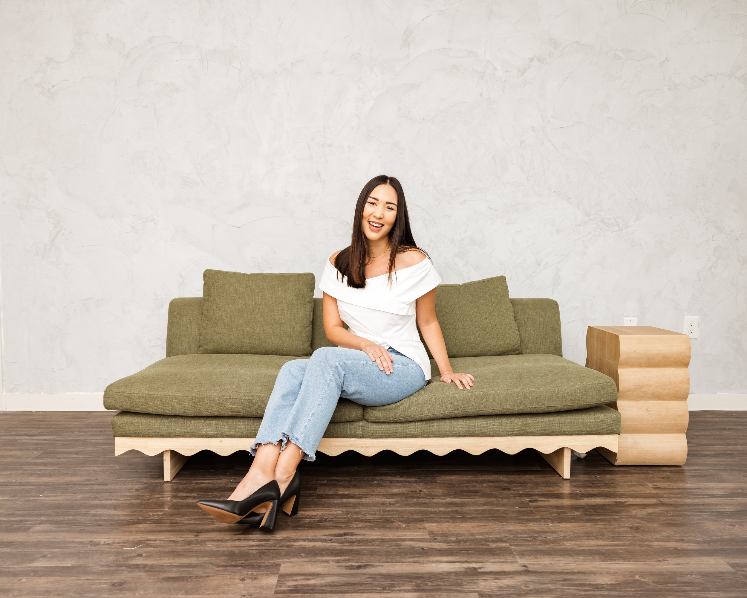 Therapist sitting on a green sofa in a minimalist office space, smiling warmly in a calm, welcoming environment.