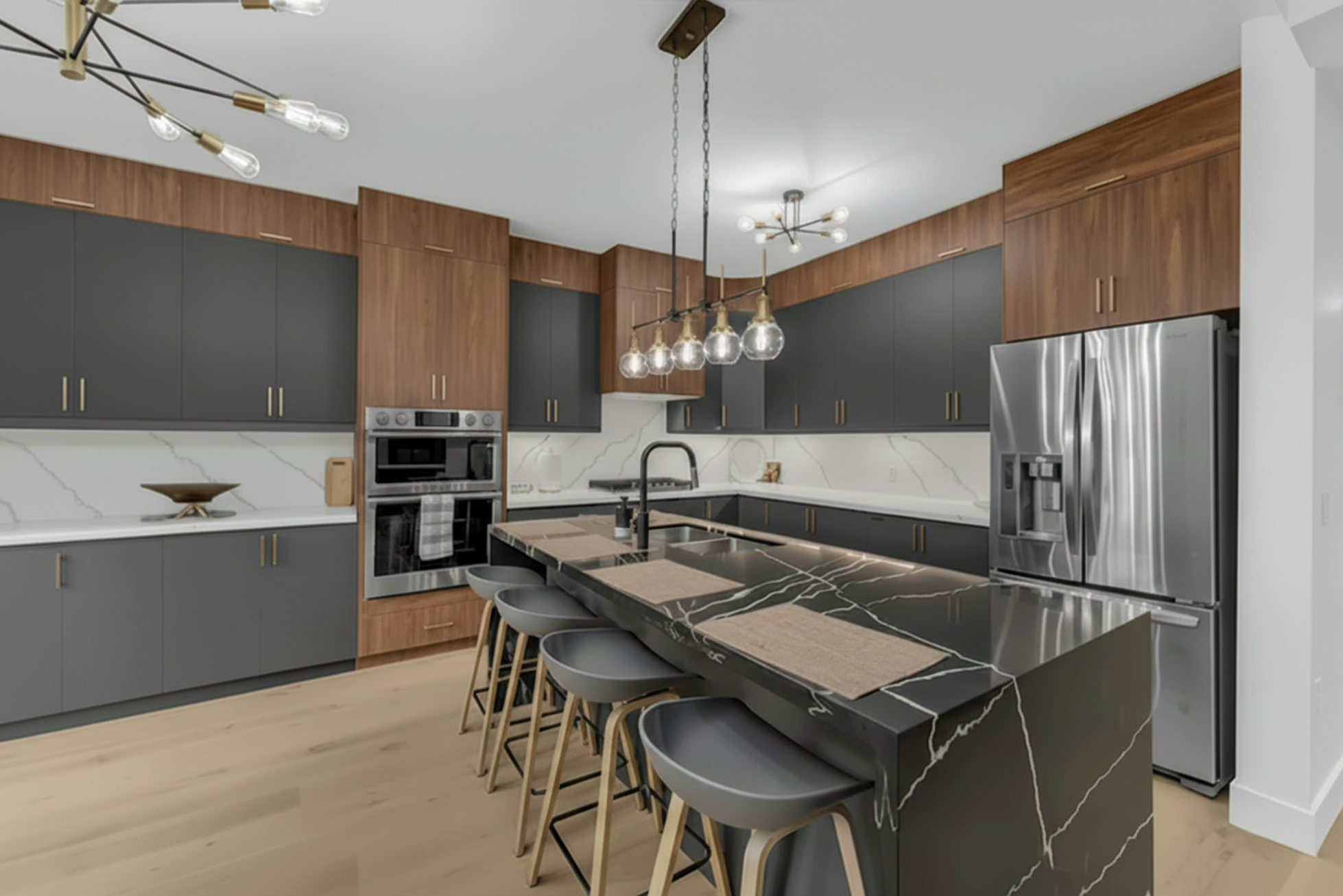 Modern kitchen with gray cabinets, black marble island with beige placemats, stainless steel fridge, and wood accents. Unique lighting fixtures are hanging from the ceiling.
