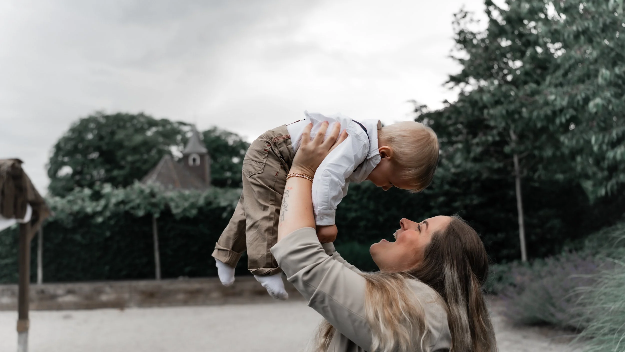 Vrouw speelt met een jonge jongen buiten in een tuin of park, terwijl ze lachen en naar elkaar kijken.