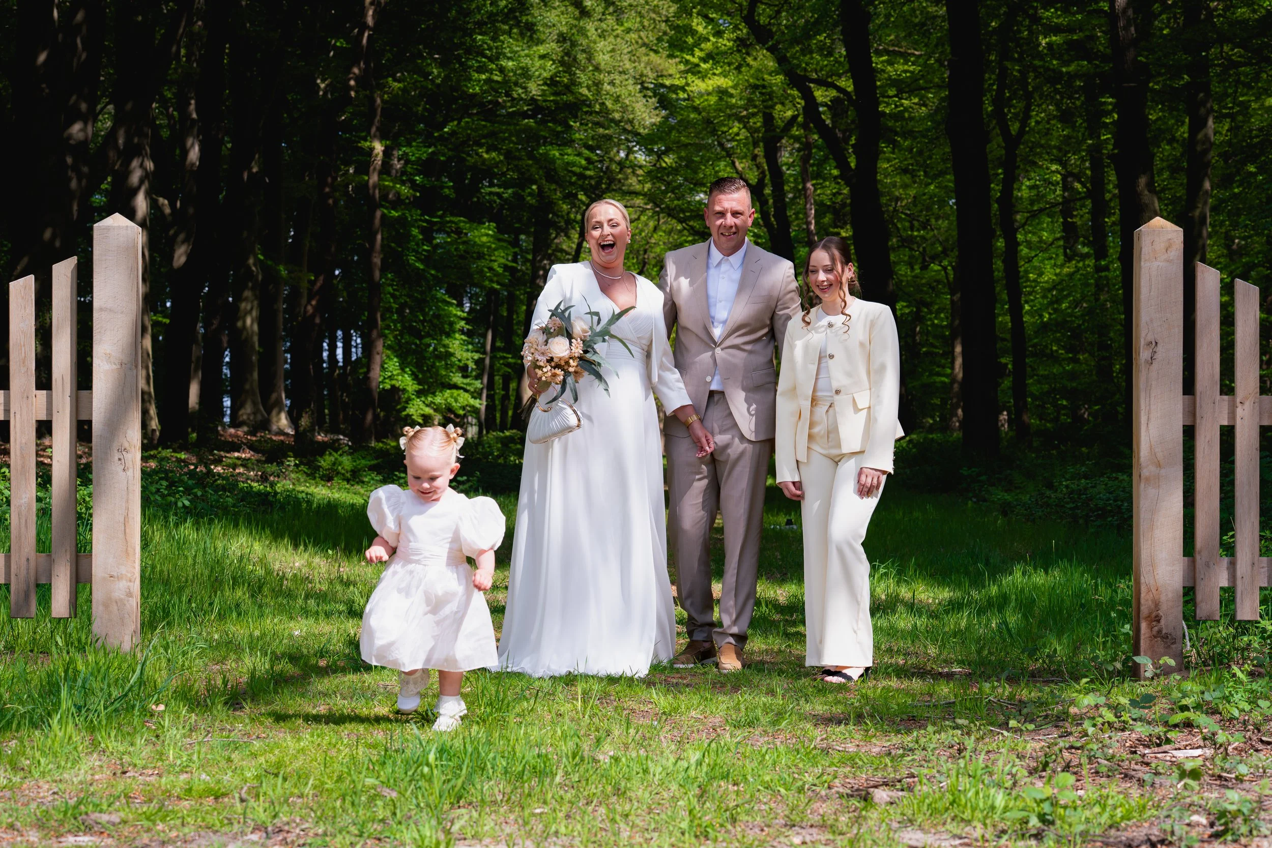 Vrouw houdt een jong kind in haar armen in een natuurlijke omgeving met bomen en bloemen op de achtergrond.