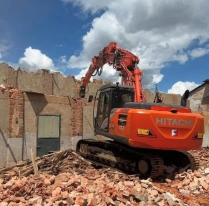 Escavatore Hitachi rosso che demolisce un edificio in rovina.