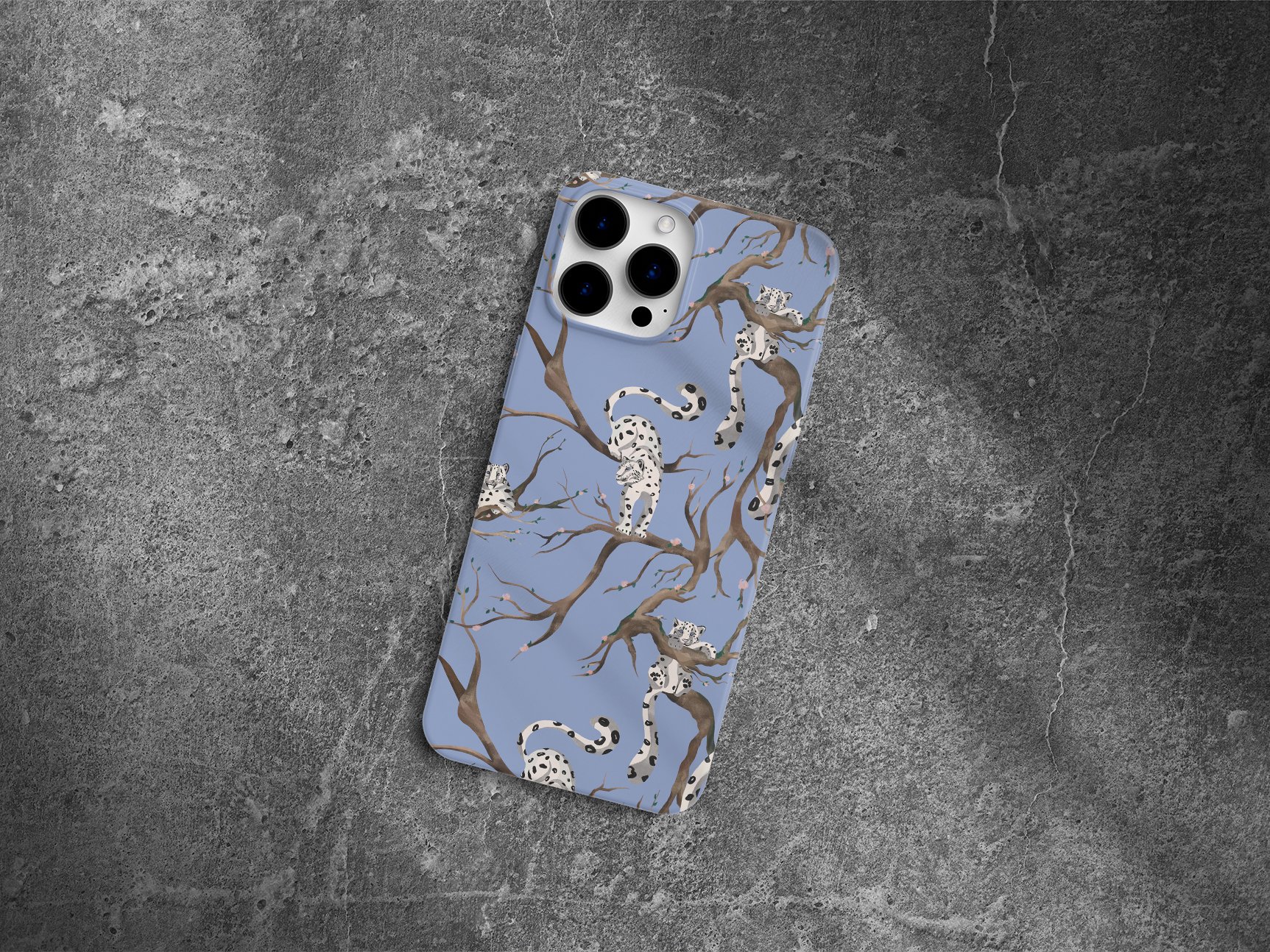 iPhone with a blue case featuring a pattern of white snow leopards climbing brown tree branches, placed on a concrete surface.