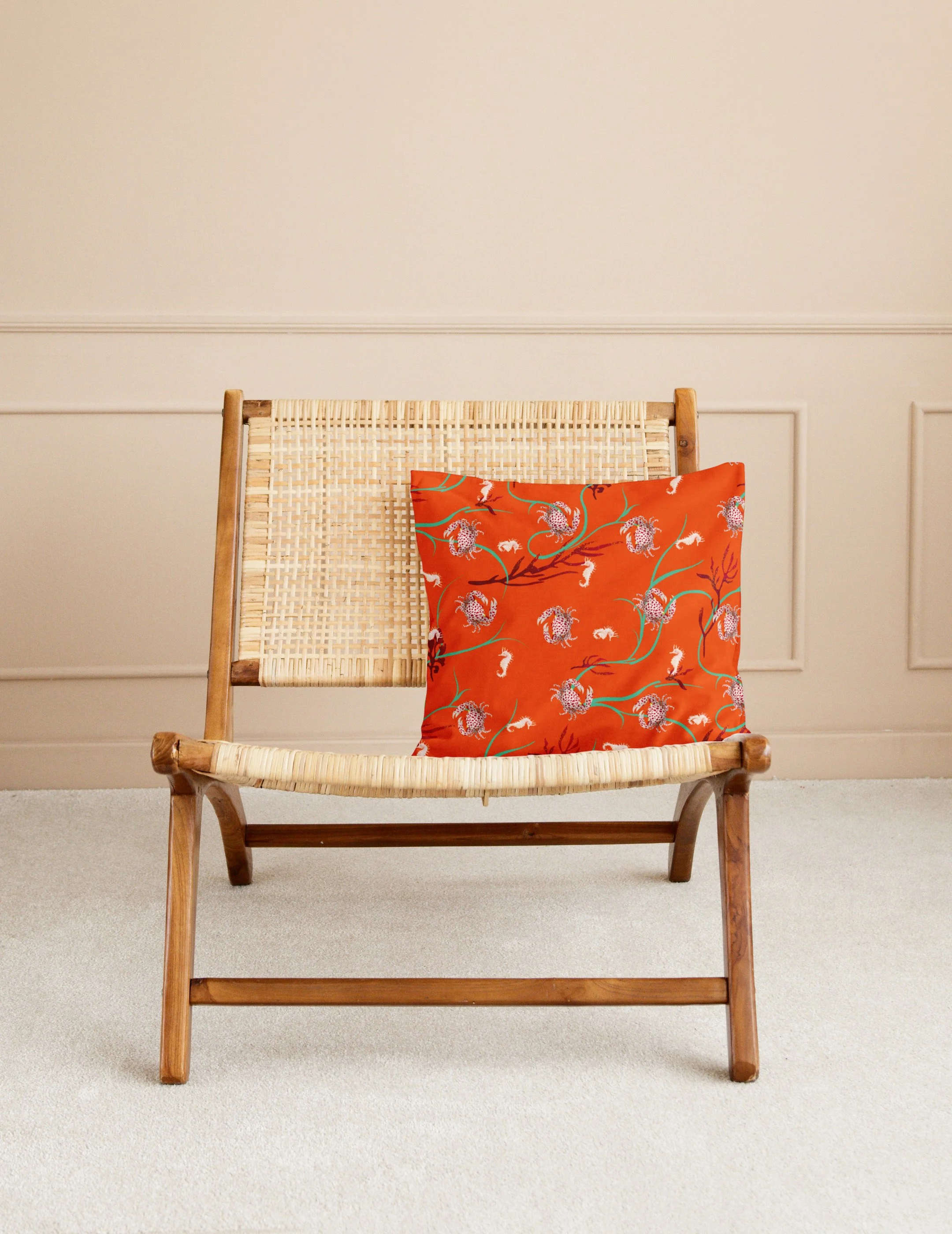 Wooden chair with woven seat and backrest, decorated with an orange floral-patterned pillow, against a beige wall with decorative molding.