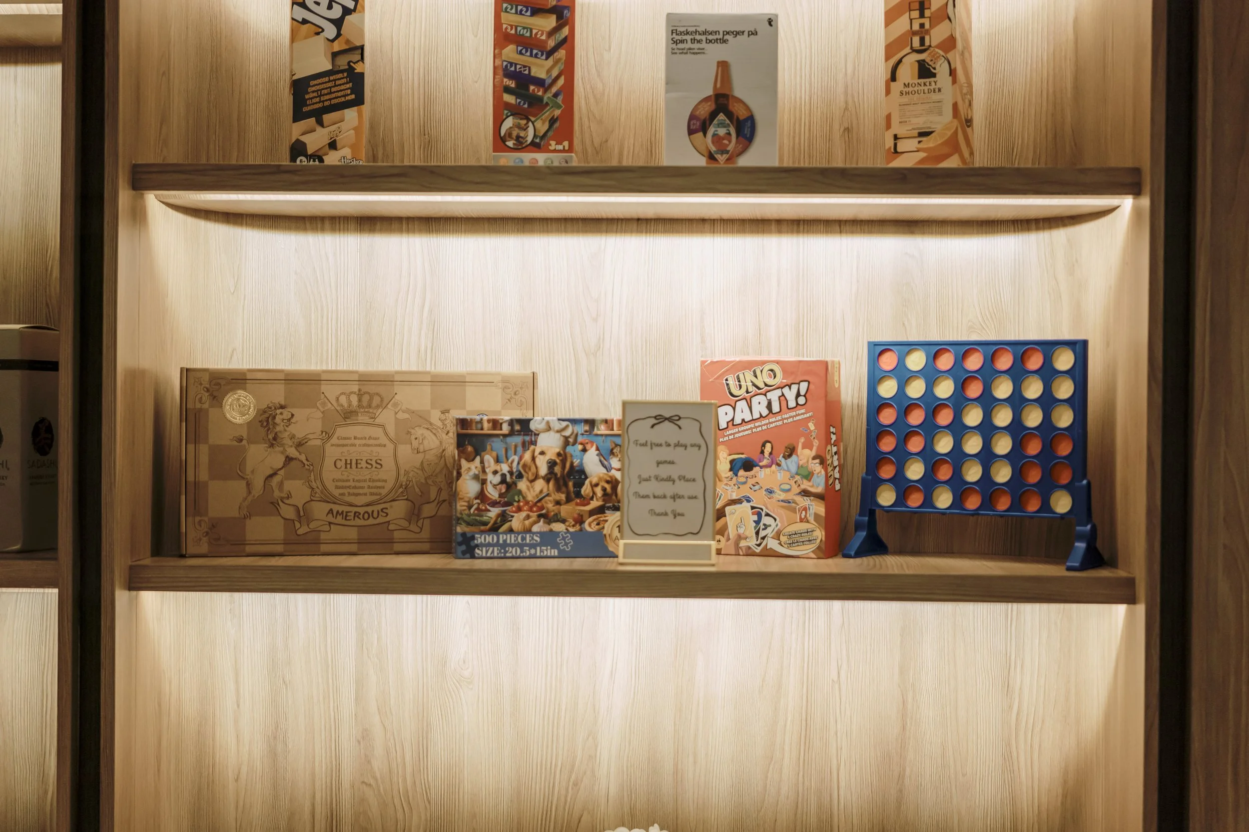 A wooden shelf with various board games and puzzles, including chess, Uno, and Connect Four and many more