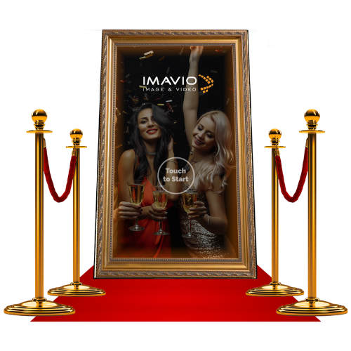 Ein digitaler Fotokabinenrahmen mit zwei Frauen, die bei einer Party lachen und Champagner trinken, eingerahmt von roten Samtseilen auf goldenen Ständern.