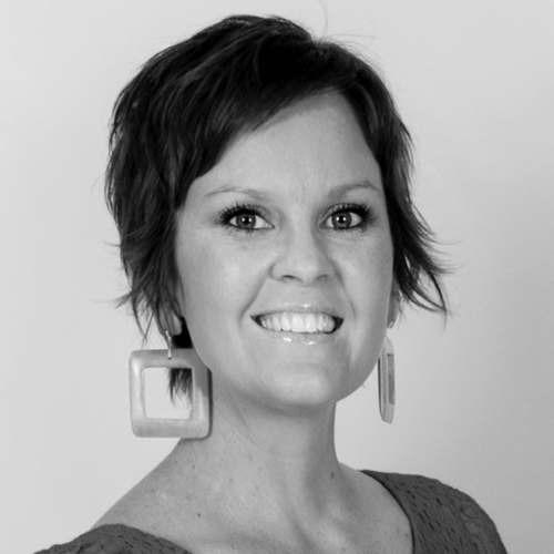 Black and white portrait of a woman with short, textured hair, smiling, wearing square earrings and a knit top.