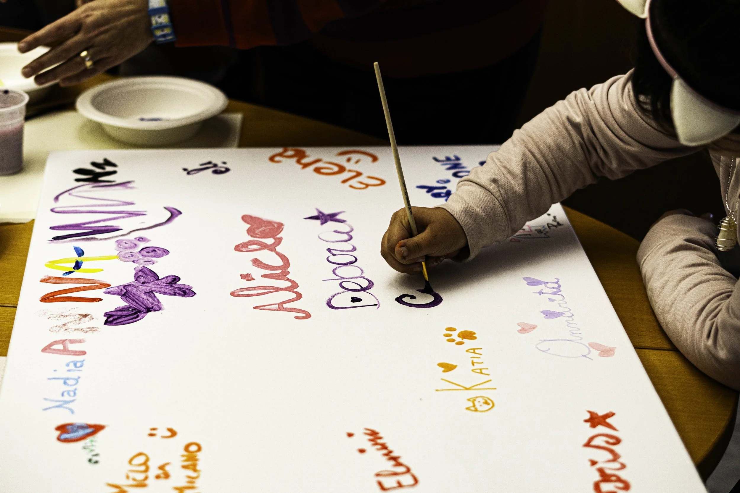Una persona sta scrivendo su un cartellone con pennarelli colorati, decorato con scritte e disegni.