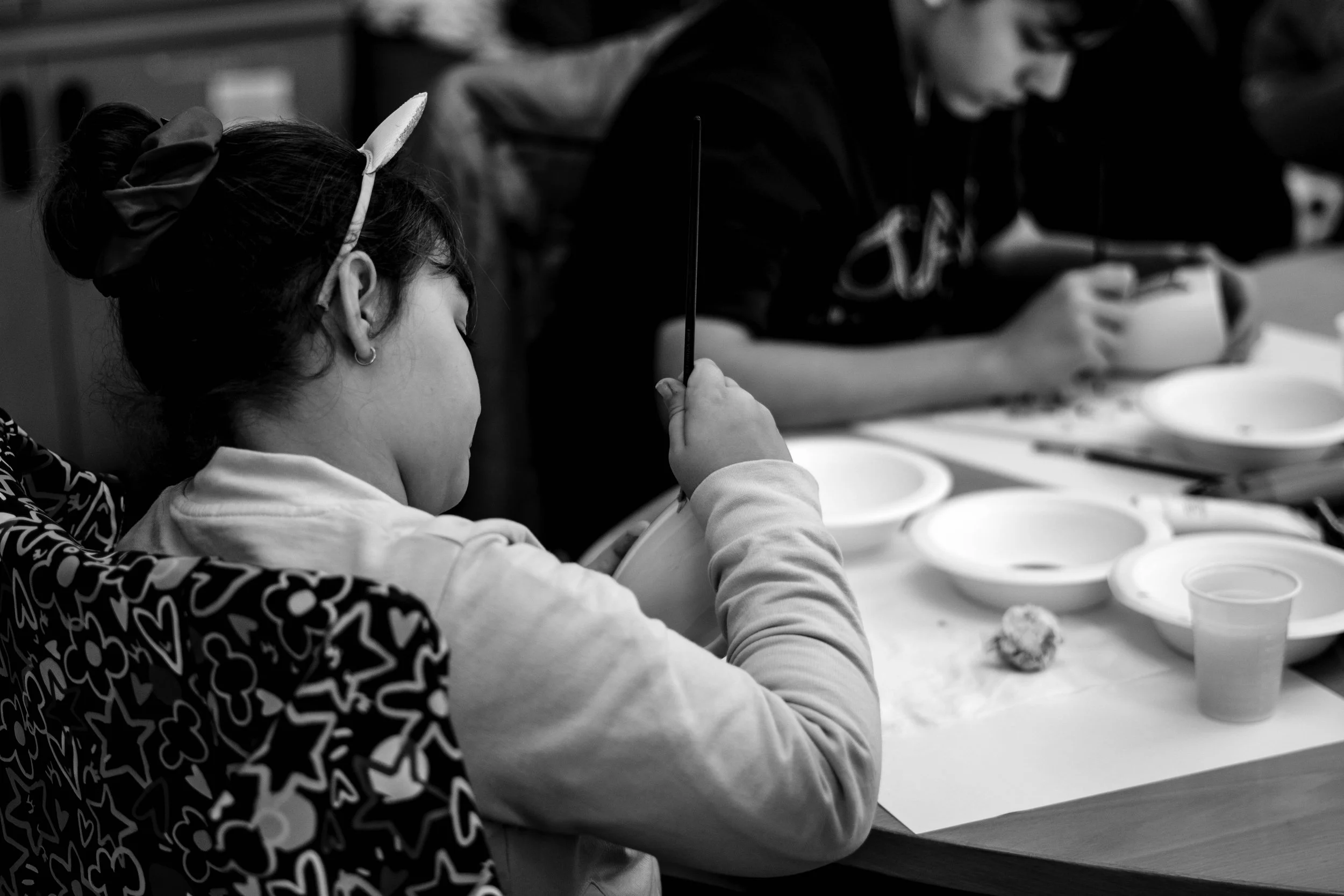 Bambina seduta con le spalle alla fotocamera, sembra mangiare o giocare con un contenitore.