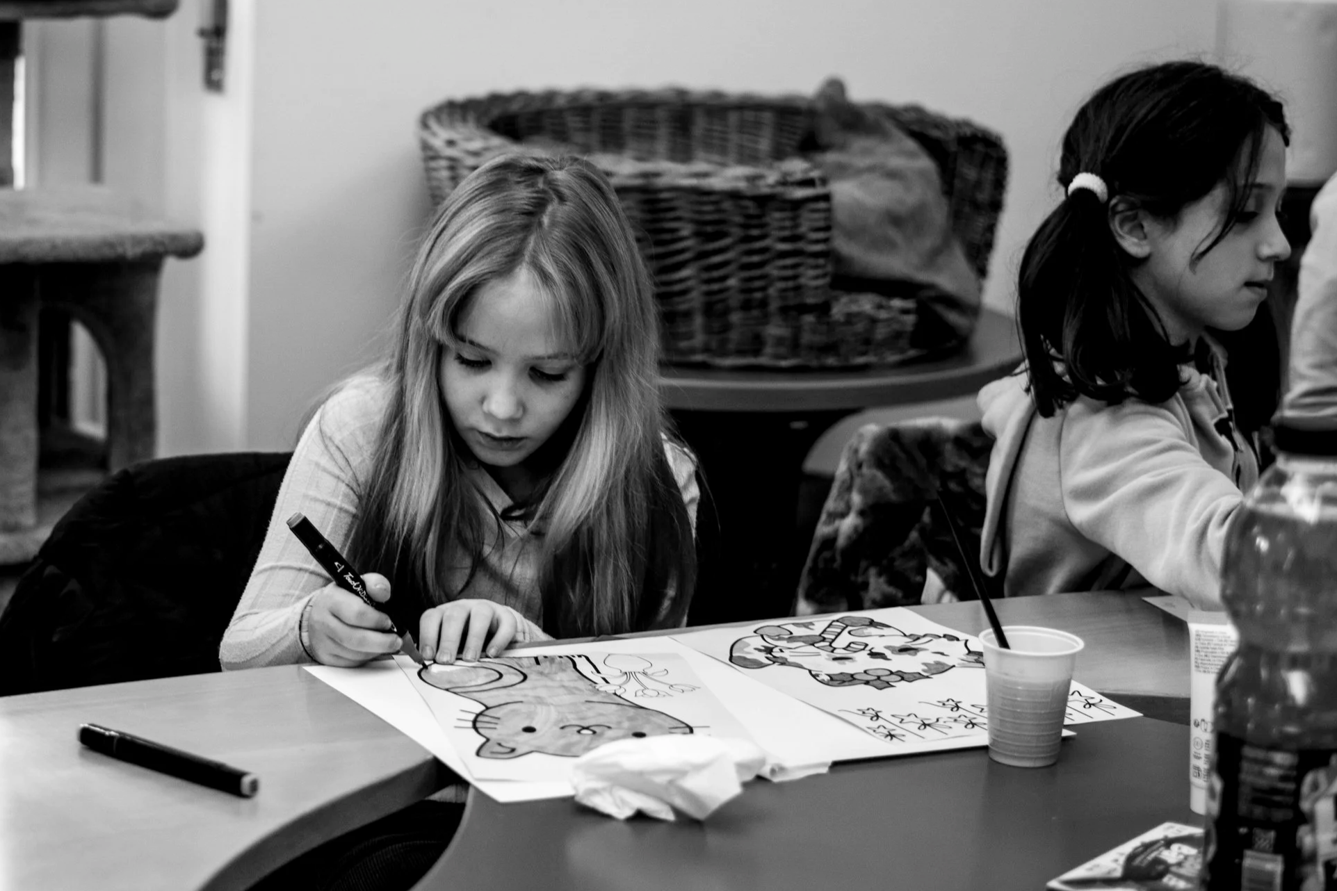 Due bambine sedute a un tavolo che disegnano e colorano dei fogli con immagini di animali.