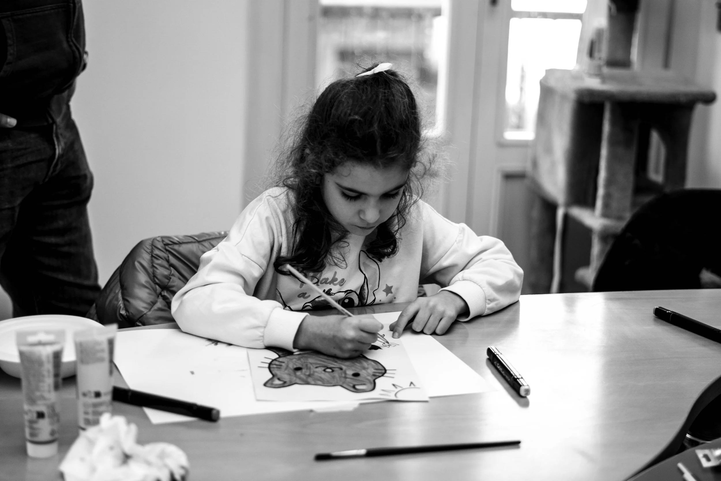 Una bambina sta colorando una pagina con il disegno di un gatto, seduta a un tavolo.