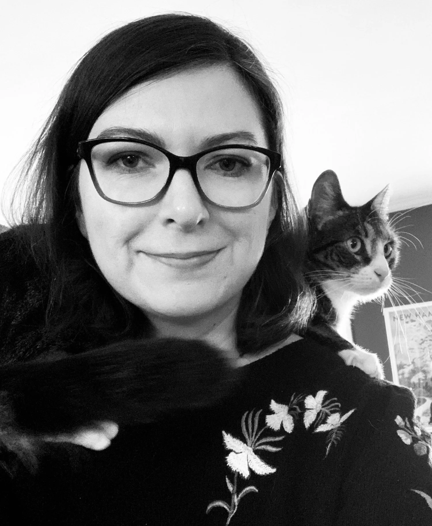 A woman with dark hair and glasses holding a tabby cat with a white chest and paws.