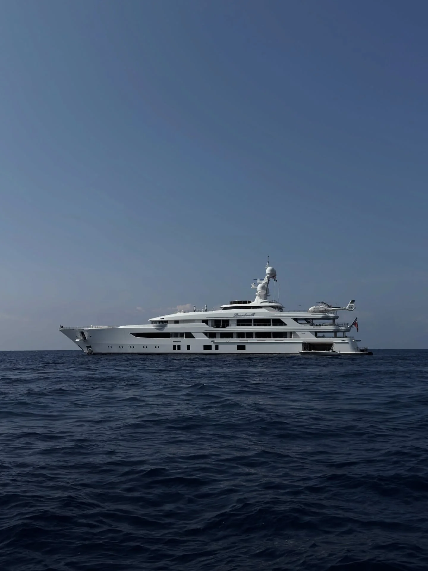 A luxury white yacht floating on the ocean under a clear blue sky