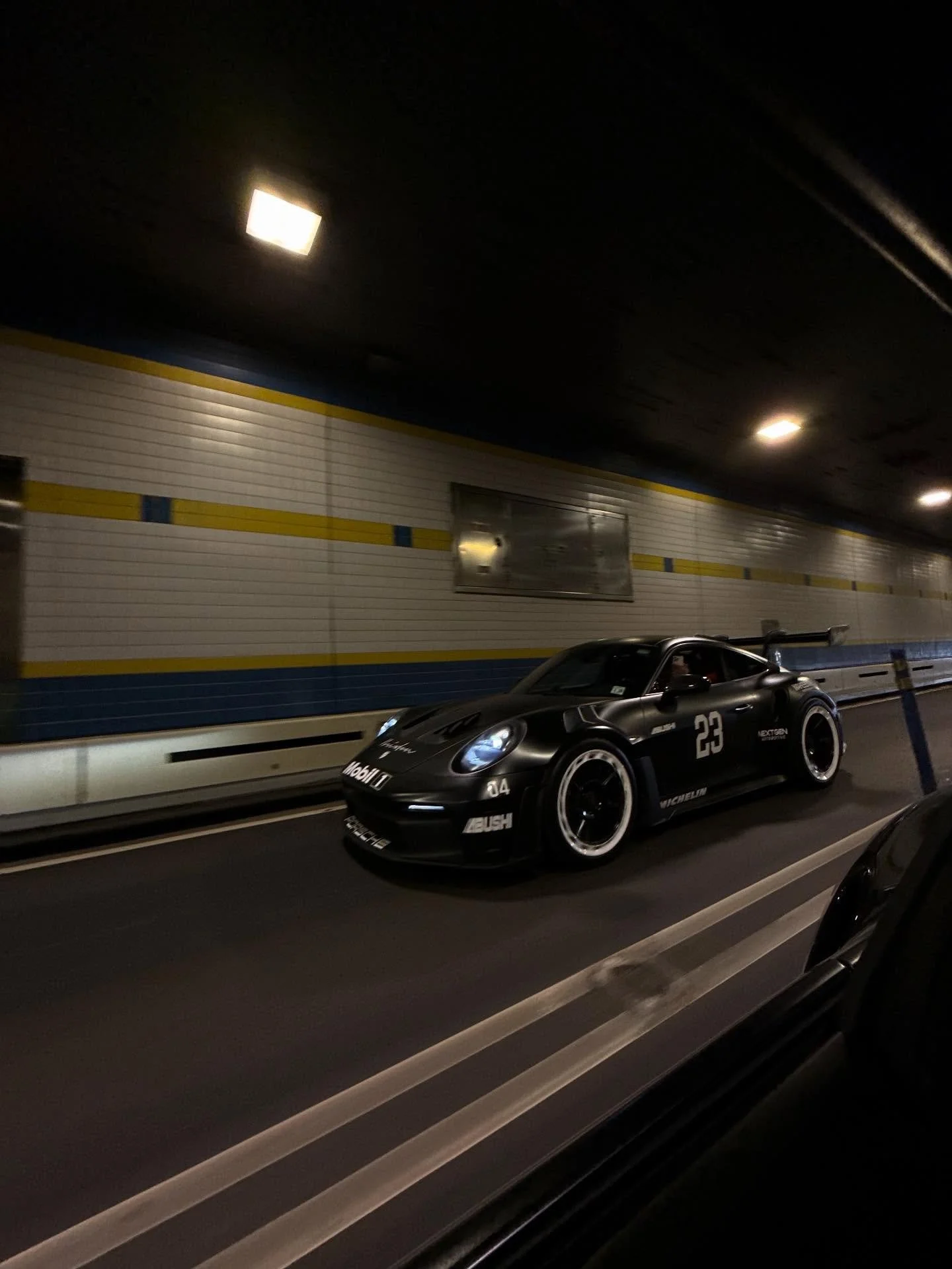 A sleek black race car with the number 23 on the side, driving on a highway tunnel at night.
