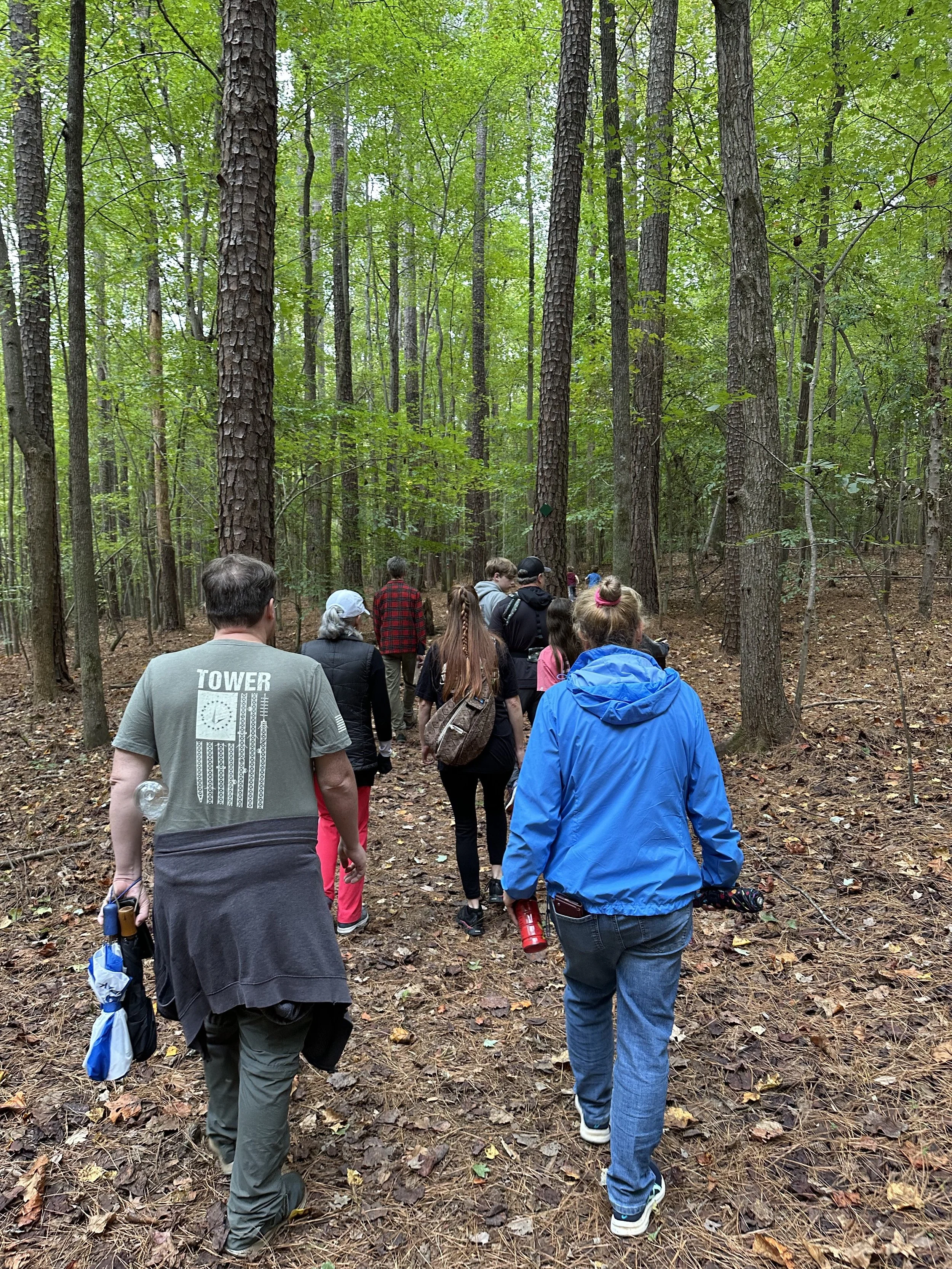 A group of people hiking along a trail through tall trees.