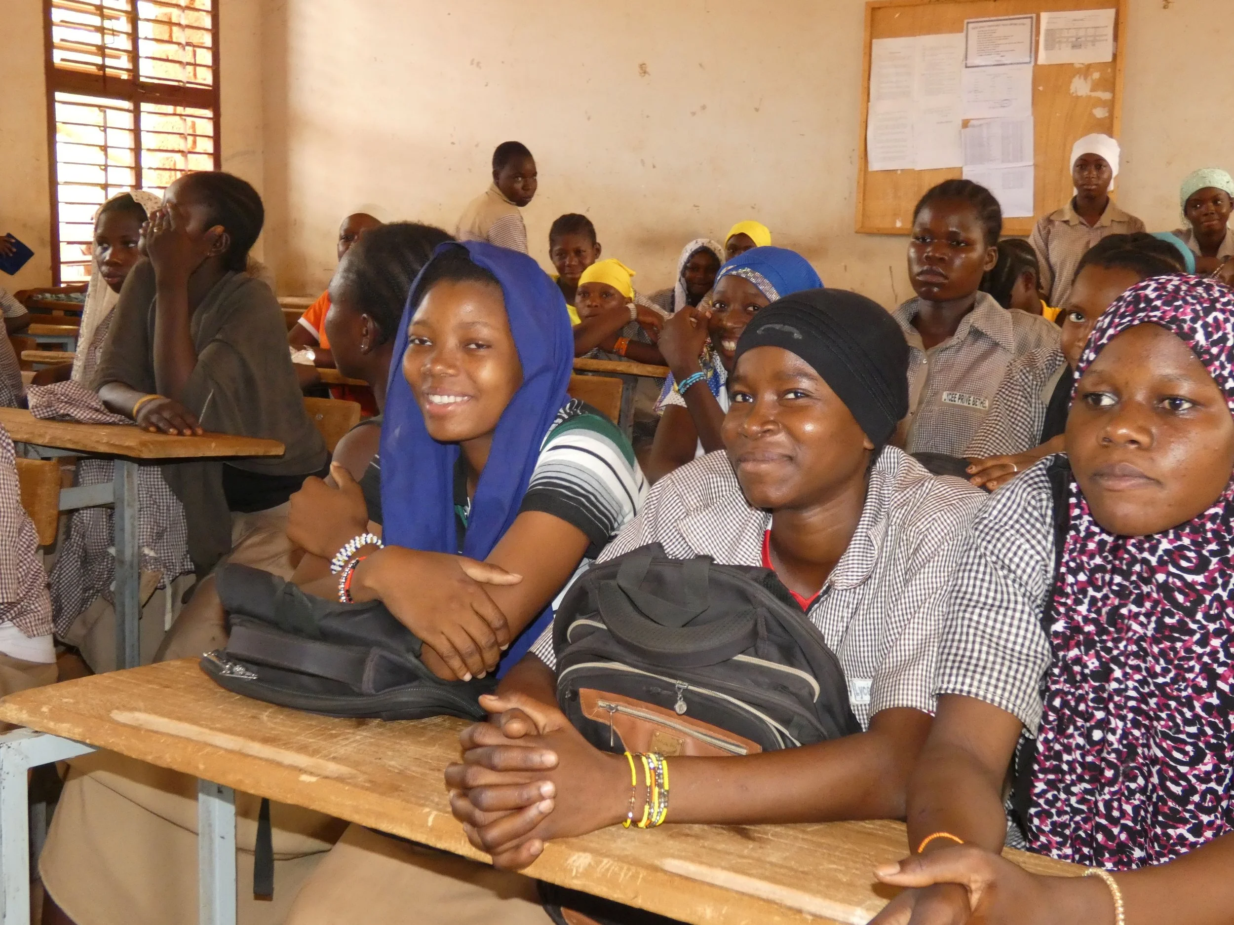 A classroom of students; two girls in the foreground are smiling at the camera
