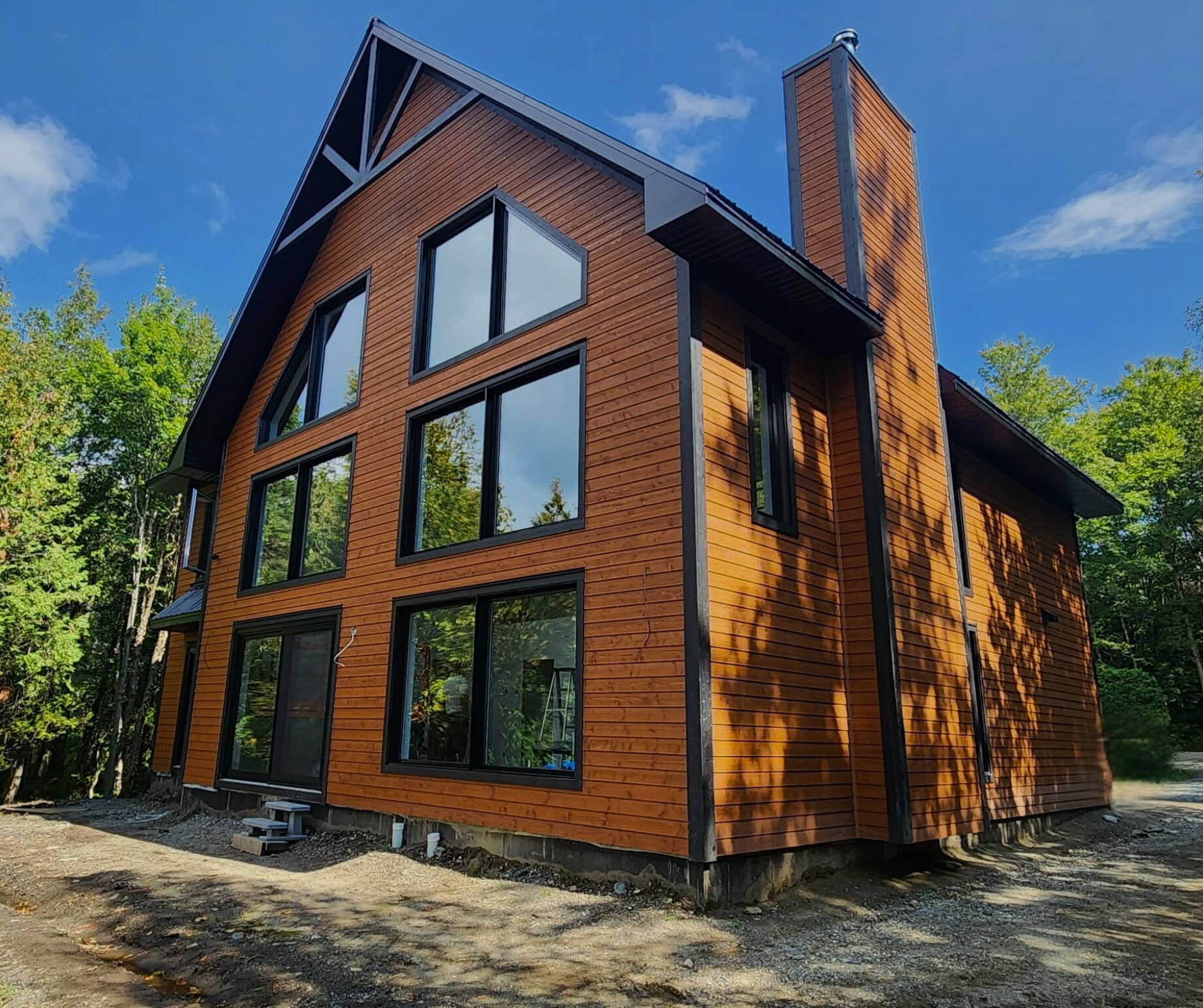 Maison en bois à plusieurs grands fenêtres dans un environnement naturel, sous un ciel bleu avec des nuages.