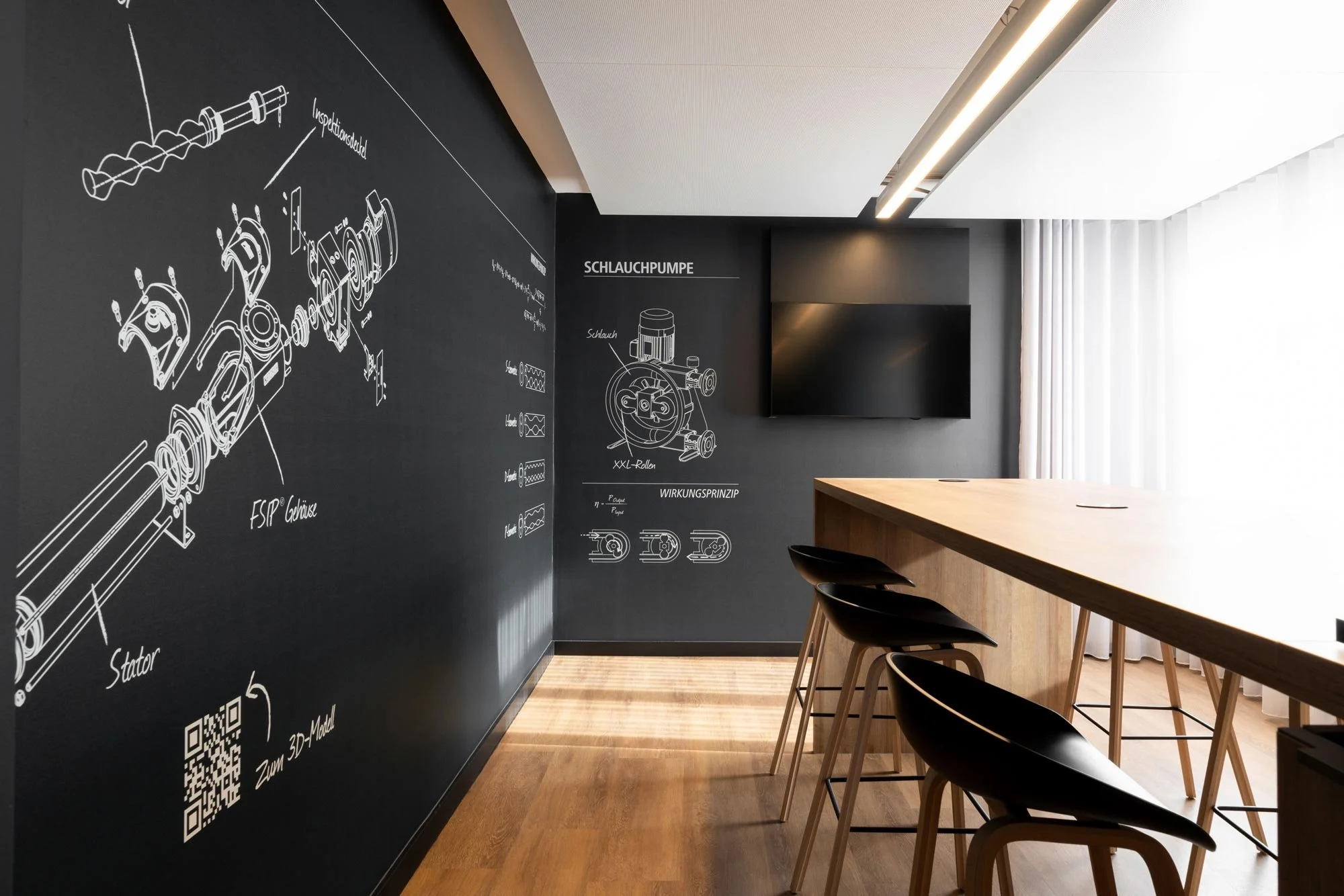 Moderne Schulungsraum mit schwarzen Wandtafeln, technischen Skizzen und Diagrammen, einem Fernseher, einem hohen Holztisch und schwarzen Stühlen, viel natürlichem Licht durch Vorhänge