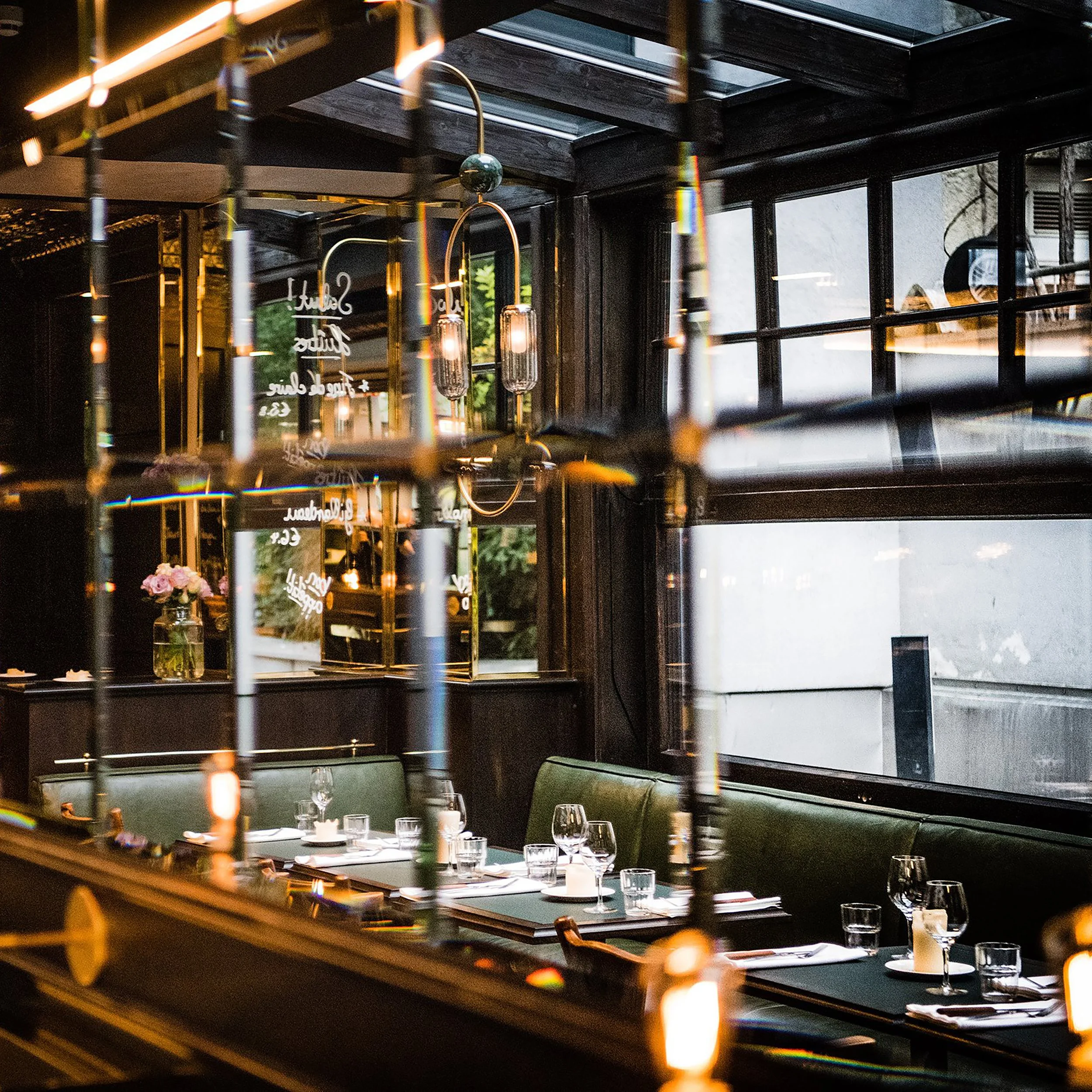 Innenansicht eines stilvollen Restaurants mit modernem Dekor, Tischen, Gläsern, Kerzen und großen Fenstern.
